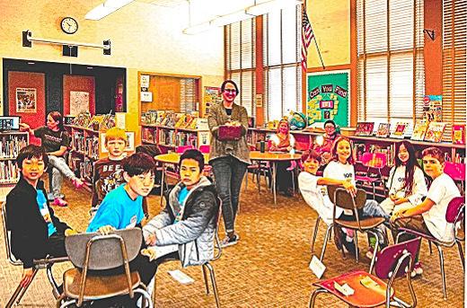 At the tournament in Woodstock Schools library, Teacher-Librarian Rosie Lingo is standing, while PTA President Kjersti Dodds is in the background monitoring the virtual streaming. Shown are the top two teams members: The Blazing Bookworms, at left  Archie, Alson, Evan, and Gus; and the Smart Smores  Theo, Clara, Emma, and Theo.