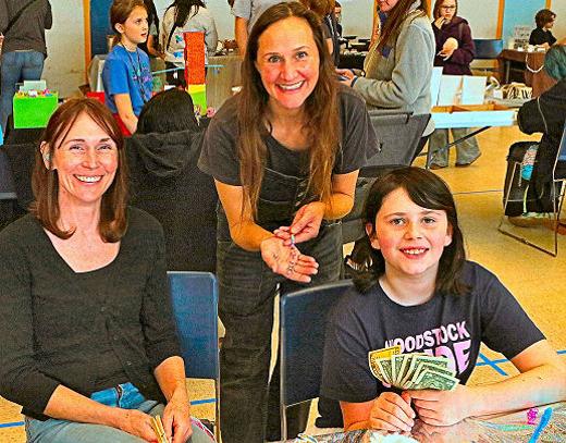 Here, Danielle Kreipe sat with her daughter, vendor Annabel Kreipe  whod just made a sale to Annie Kobliska-Becker, and had the cash to show for it!  at the 2025 Portland Mini-Makers Market on March 1st, inside the Woodstock Elementary School gym.