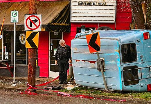 A Central Precinct officer examined the smashed and wedged-in van, while waiting for a second and larger tow truck to arrive to remove it from the sidewalk on Milwaukie Avenue near S.E. Nehalem Street in Sellwood.
