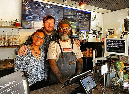 At Woodstocks Sign Language Café, two baristas  Rae Davis, left, and Max Pool in back, stand with Café Manager and Operator Dre Gray. The speech-to text screen, at right, registers customers speech, to assist the Deaf and hard-of-hearing.