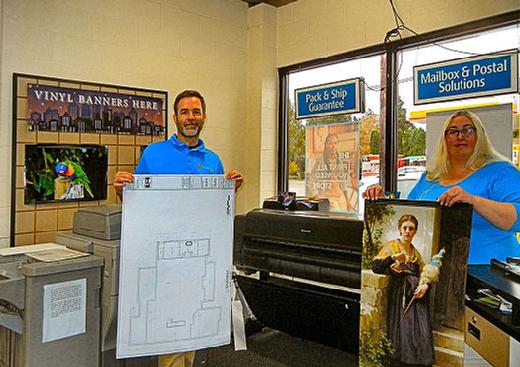 With the new Canon production printer in the background and a photo print of parrot at left, Woodstock UPS Store owner Kelly Keogh holds a sample architectural plan printed on it, and Printmaster Terill Ketcham holds a sample of its fine art reproduction.